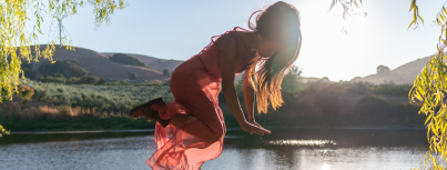 Image of company member Miche Wong in an orange dress floating among the McEvoy landscape with leaves surrounding her